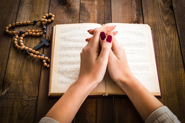 Folded hands praying over the bible. On a wooden background.