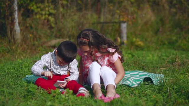 Little children play with a mobile phone in the garden
