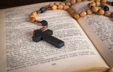 Bible and a rosary with a cross. On a wooden background.