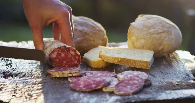An experienced chef in a professional kitchen cuts the salami seasoned.Il Italian salami sausage is cut with a professional knife with very thin slices. the concept of nature, Italy, food, diet and bi
