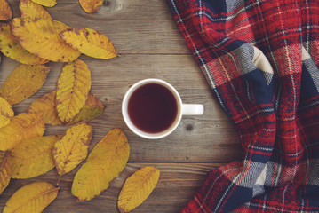 Flat lay view of autumn leaves and tartan textured scarf on wood