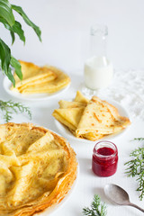 Thin pancakes, jam and milk on white table