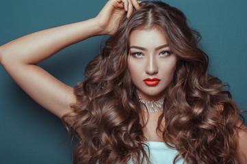 Fototapeta premium Glamour portrait of beautiful woman with fresh evening makeup and romantic wavy hairstyle. Fashion shiny highlighter on skin, sexy gloss red lips make-up and dark eyebrows