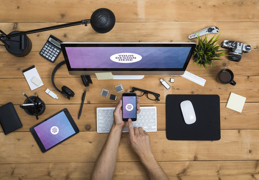 User with Desktop Computer, Tablet, and Smartphone on a Cluttered Wooden Table Mockup 2