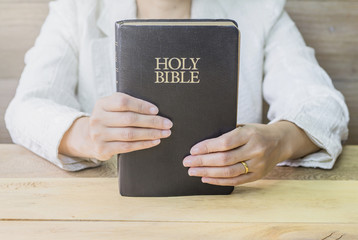 a woman hands holding the holy bible over wooden table