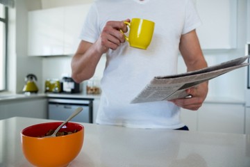 Man reading newspaper while having coffee in kitchen