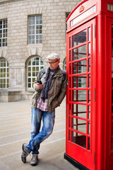 Tourist in England standing at the red telephone box. He is sending message.