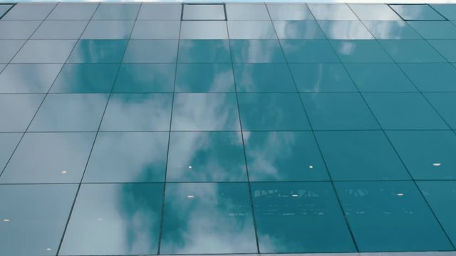 Reflection of blue sky and white clouds on the mirror surface of the glass windows in high-rise building. Dolly shot