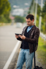 Fototapeta premium man standing with digital tablet waiting for car or taxi. Hitchhiking