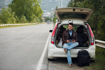 leisure, road trip, travel and people concept - happy man searching location using tablet with online map sitting on trunk of hatchback car outdoors - obrazy, fototapety, plakaty