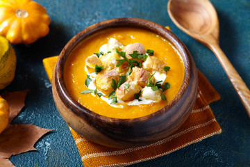 Pumpkin and carrot soup with cream and parsley for Thanksgiving, halloween. On blue creative background. Composition of autumn vegetables.