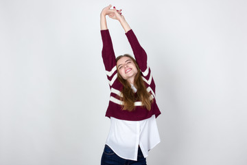 Portrait of a pretty woman  in short sweater, white shirt and jeans stretchingstanding and smiling over gray background