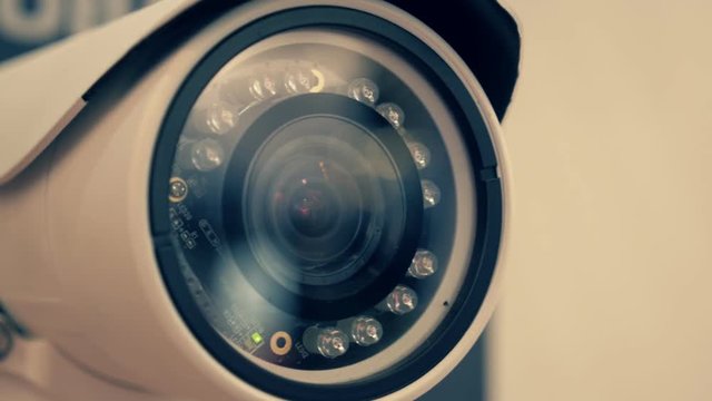 White security camera is checking the surrounding area in search of the offender. Blinking red bulb means recording going. Shot in motion