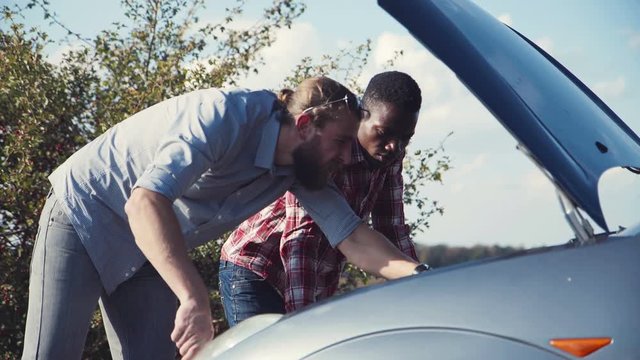 Two men trying to fix their car standing on roadside in countryside.
