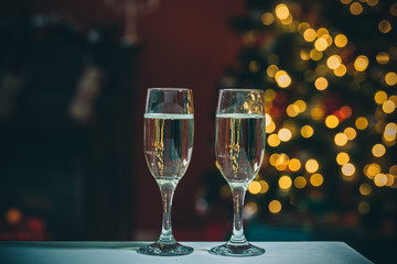 Beautiful two glasses of champagne standing on the table in the background of a blurred room with a decorated Christmas tree and fireplace. Soft focus. Shallow DOF