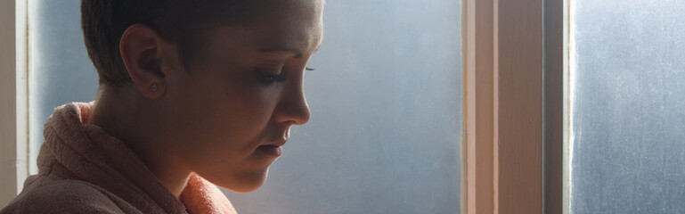 Young cancer patient standing in front of hospital window