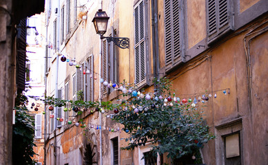 A quiet old traditional street in Rome with old facades and windows with wooden shutters and christmas toys hanging from side to side of the street. 