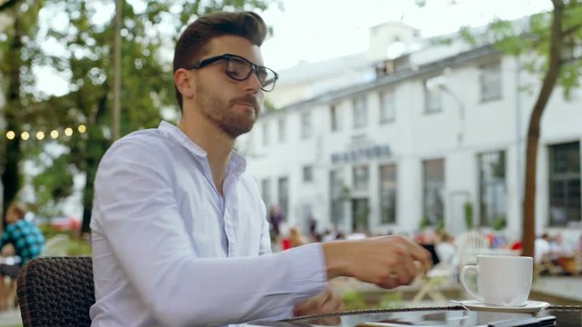 Man drinking coffee in the outdoor cafe and opens laptop 
