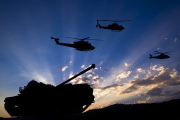 Fototapeta na wymiar Military tank and helicopters silhouetted against dawn or dusk blue sky