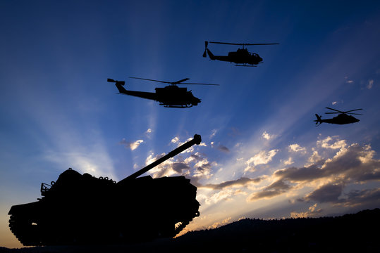 Military tank and helicopters silhouetted against dawn or dusk blue sky