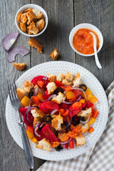 Salad with peppers, tomatoes, onions, olives and croutons with sauce old wooden background. Selective focus.