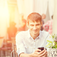 Young man with smartphone sitting at the cafe