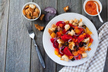 Salad with peppers, tomatoes, onions, olives and croutons with sousomna old wooden background. Selective focus.