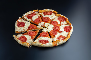 Cut into slices delicious fresh pizza on a dark background. Pizza on the black table.