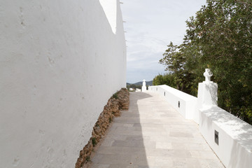 Gehweg mit Steinplatten und weißer Mauer und Kirchenkreuz