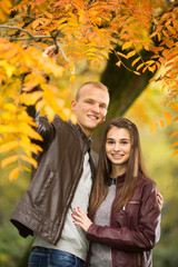 Young couple are enjoying therig time together in a park on a beautiful Autumn day. They are looking to camera.