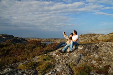 Couple taking a selfie on large stone covered with colorful lichens at a coastal heathland at a hiking path next to Marstrand, Kungälv Municipality, Västra Götaland County, Sweden