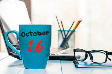 October 16th. Day 16 of month, morning tea in blue cup with calendar on banker workplace background. Autumn time. Empty space for text