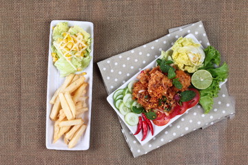 Spicy sour fried chicken salad (Yum Kai Zap in Thai) served with a dish of mixed vegetables salad and french fires.