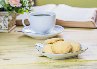 cookies with a white cup of coffee and book on wooden table
