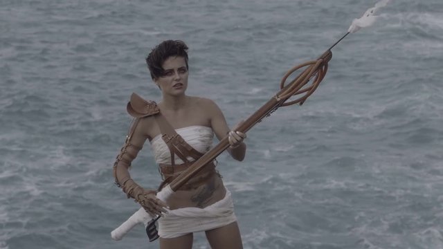 Beautiful amazon woman warrior wearing white outfit and brown leather swordbelts standing on the rocks with rifle and shooting over stormy sea background