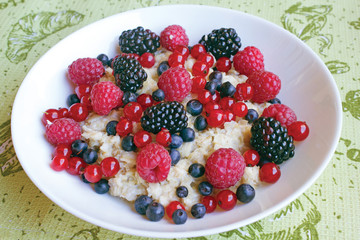 Milk porridge with different berries in a white plate on a green background