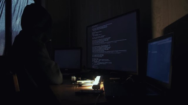 Hacker in hood cracking code using computers in dark room
