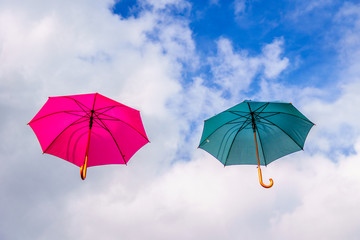 Pink and green umbrella or parasols floating suspended in the air under cloudy sky