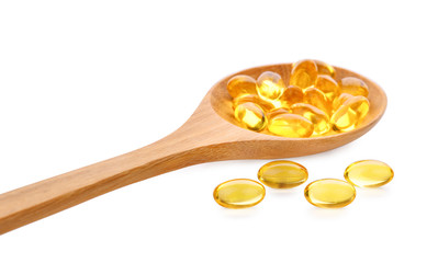 Fish oil pill in wooden spoon isolated on white