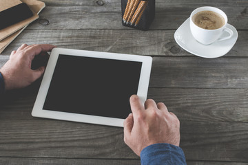 Men presses screen tablet sitting at a wooden table