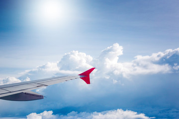 cloudy sky and red airplane wing as seen through window on aircr