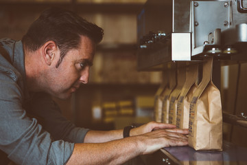 Worker looking at line of packed coffee beans - obrazy, fototapety, plakaty