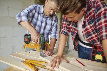 Senior carpenter is drilling  wooden planks.