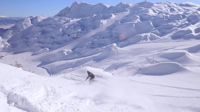 FOLLOW: Snowboarder having fun riding powder snow, jumping over mountain bumps