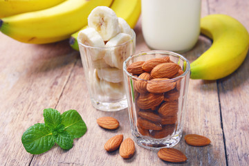 Almond nuts and sliced banana in glass with almond milk in bottle.