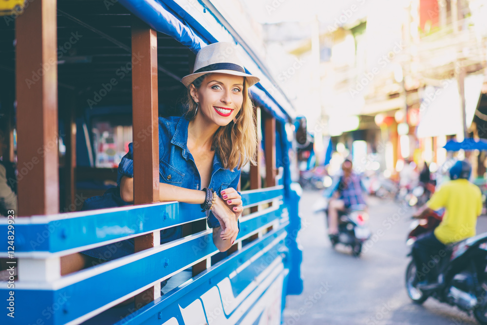 Wall mural Traveling Asia. Young pretty woman in hat enjoying trip in traditional thai bus.