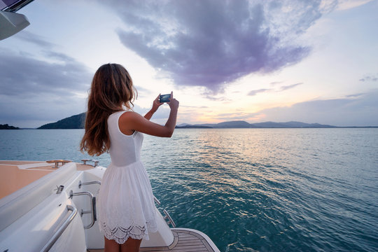 Luxury travel on the yacht. Young woman taking photo of beautiful sea lagoon on smartphone.