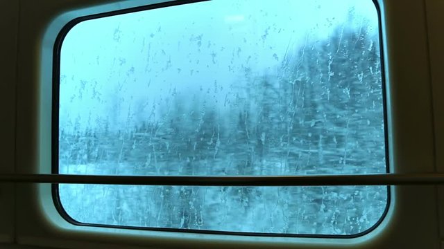 Train quickly goes through a winter forest. Train window with frozen streams of water. The view from the window. Seamless loop