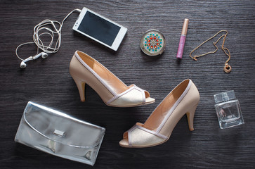 Must have for party night. Overhead of essentials for modern young woman. Different objects on wooden background: silver clutch, smartphone, heels and parfume.