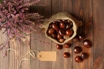 Heathers in ceramic pots, horse chestnuts in jute bag and tag on background of dark wooden boards